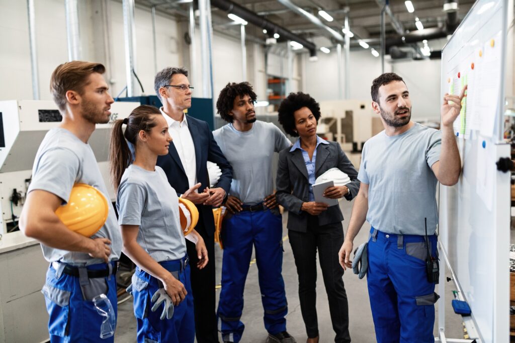 A group of intern and trainee engineers listening to a technical trainer presenting information on a whiteboard in an industrial training facility.